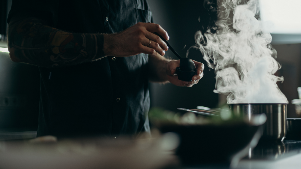 A chef stirs a steaming pot in a dimly lit kitchen.